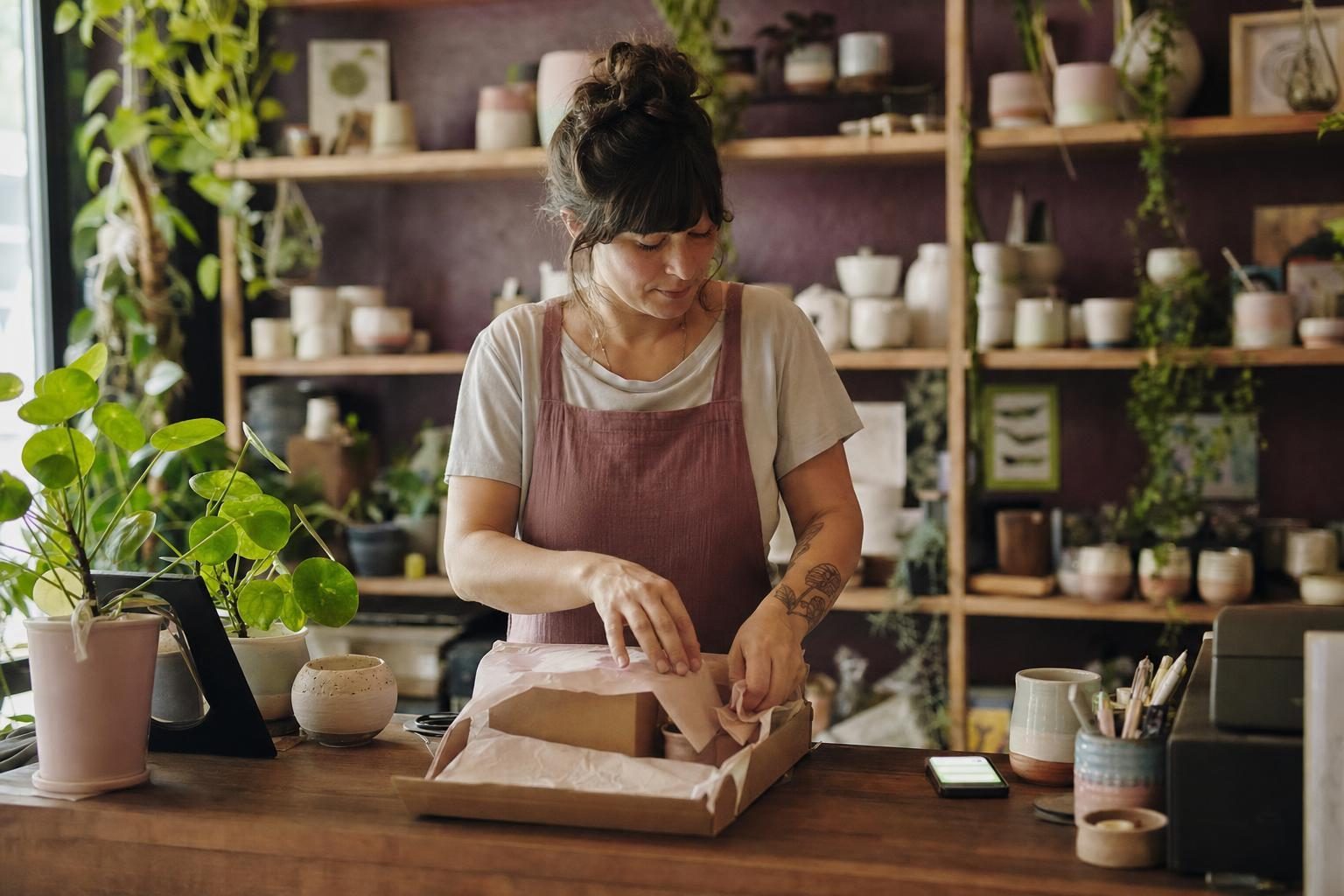 Independent shop owner packing an order while customer messages arrive on a phone